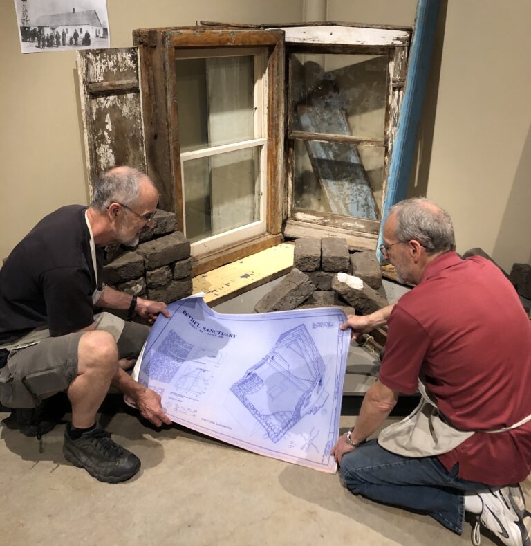 Jim Mueller and David Kreider work on a section of the new Kauffman Museum exhibit that comprises a piece of the old adobe church in Buhler, Kan.