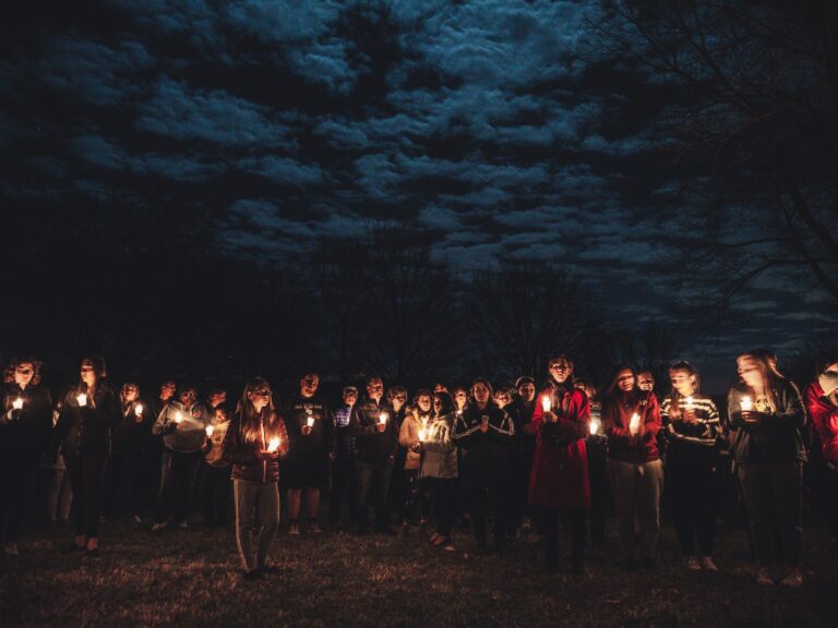 People holding candles under a moonlit sky