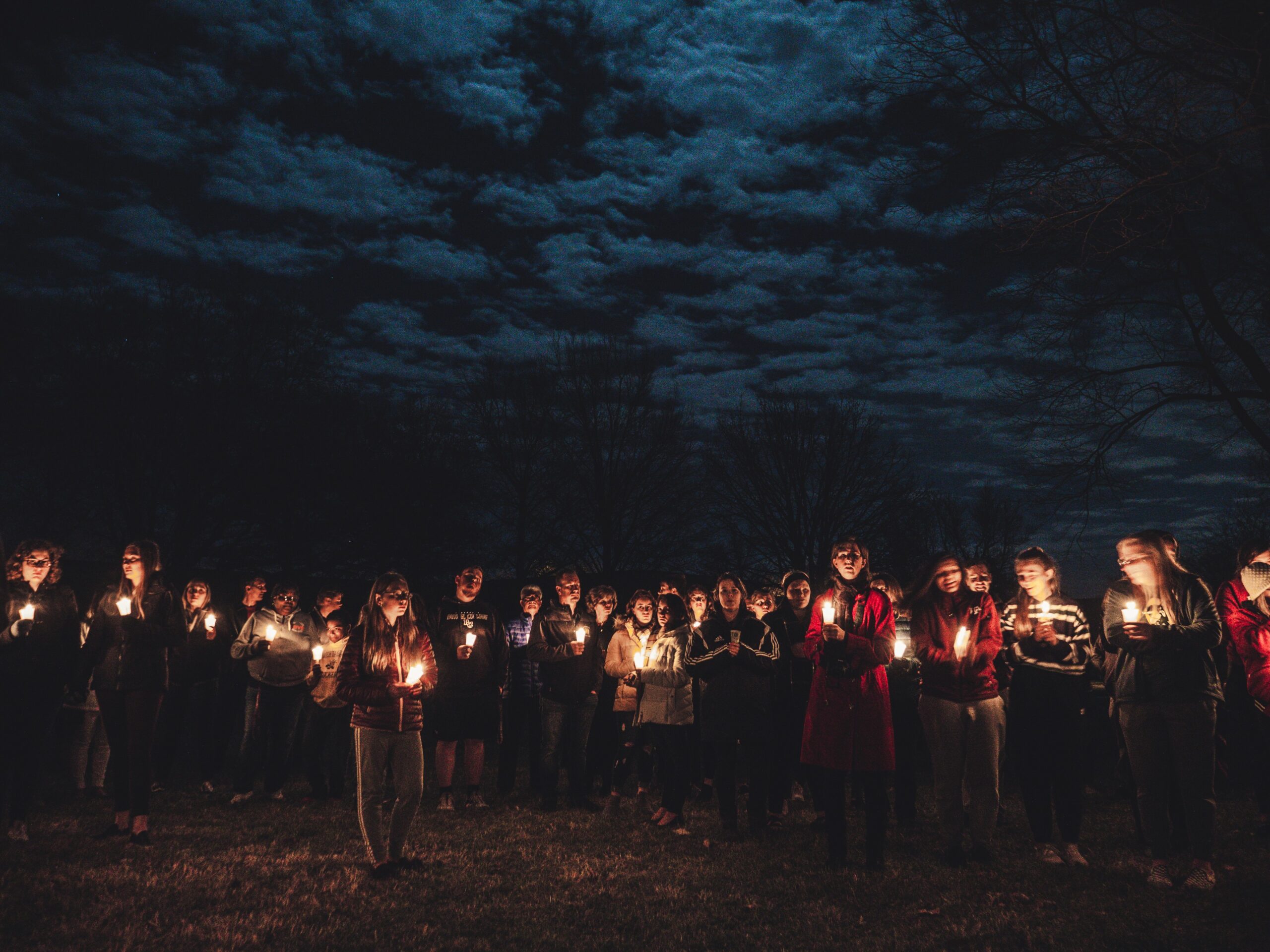 People holding candles under a moonlit sky