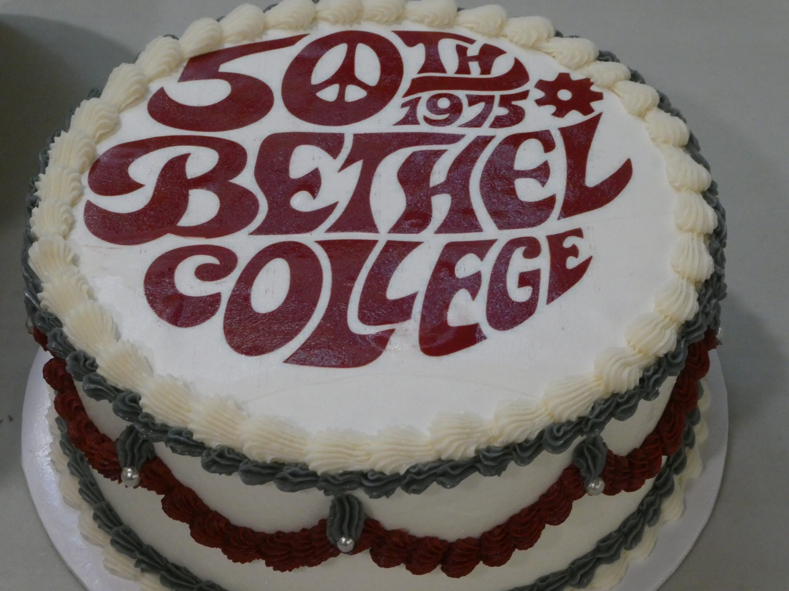 Round cake with white frosting and Class of '75 logo in maroon