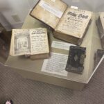 Three books inside a plexiglass display case, with identifying text.