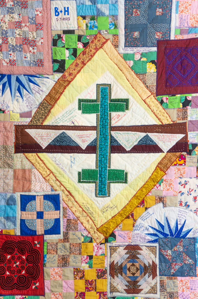 Detail of fabric art by Hattie Lee Mendoza, with a turquoise cross "reflecting" a second cross, with quilted designs around them