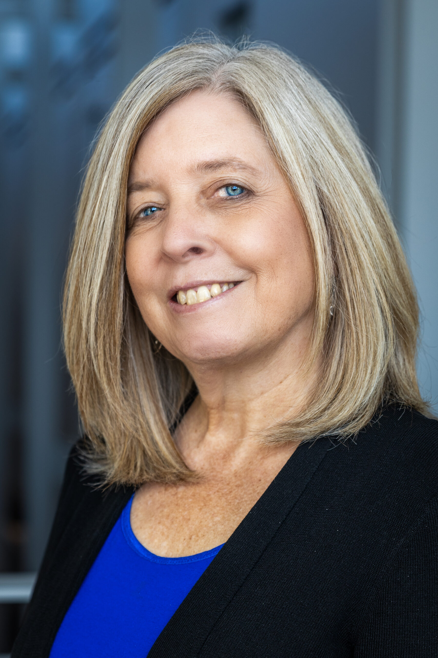 Headshot of woman with long blonde hair, wearing a black jacket and dark blue shirt