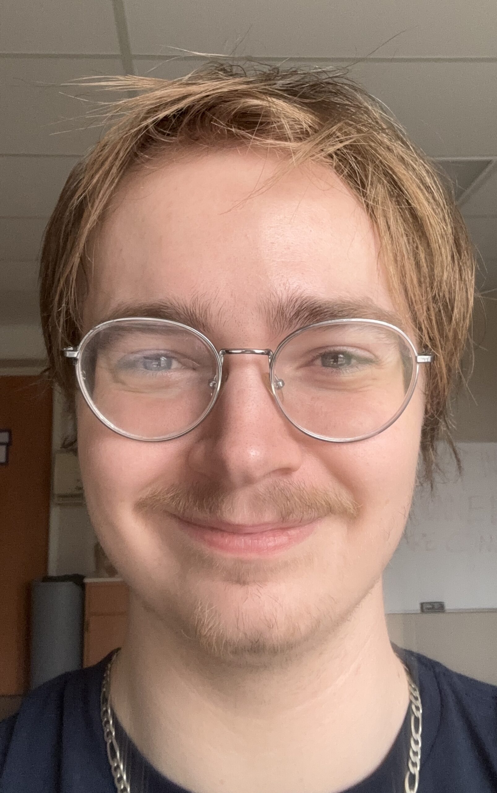 Headshot of Preston Vicenzi, young white man wearing round-frame glasses, black T-shirt and silver chain